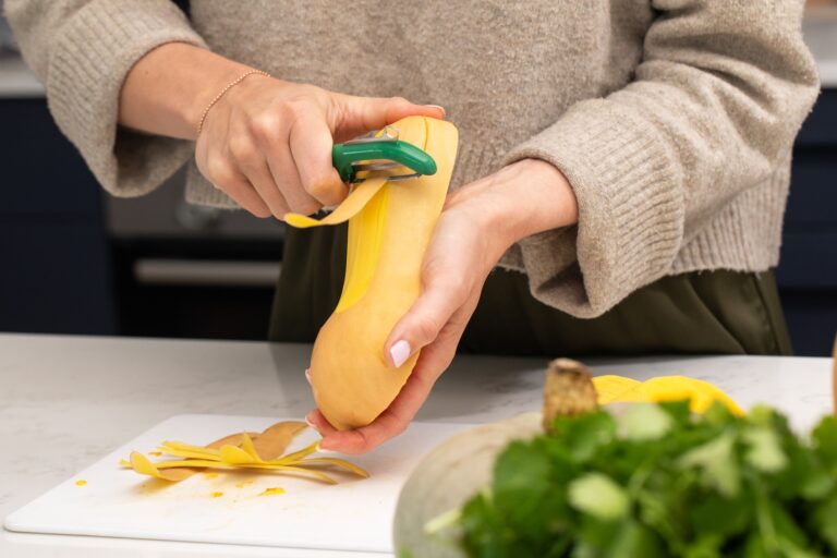 Female adult peeling butternut squash in kitchen with varieties of gourds. Pumpkin, autumn
